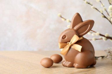 Çikolatalı Paskalya tavşanı, söğüt dalları ve tahta masada açık gri arka planda yumurtalar, yakın plan. Metin için boşluk