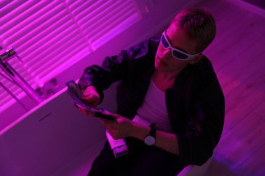 Ceketli ve güneş gözlüklü genç işadamı içeride mor ışıkta küvette para sayıyor.