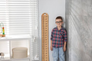 İçerideki ışık duvarının yanında, boyunu grafikle ölçen küçük çocuk.