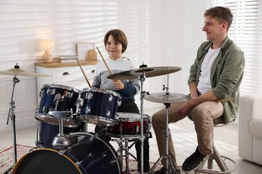 Küçük çocuk içeride müzik öğretmeniyle davul çalmayı öğreniyor.