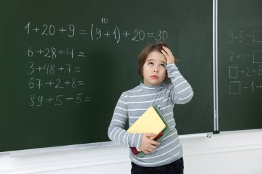 Matematik ödevi olan, karatahtanın yanında defterleri olan okul çocuğu.