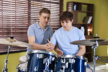 Genç çocuk içeride müzik öğretmeniyle bateri çalmayı öğreniyor.