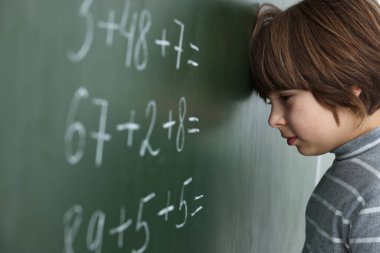 Okullu çocuk sınıfta tahtada matematik yapıyor.