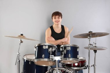 Gri arka planda davul setiyle gülümseyen genç çocuk.