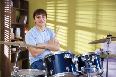 Elinde bagetlerle ve davul setiyle gülümseyen genç çocuk.