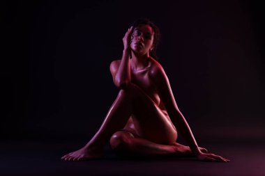 Güzel çıplak kadın karanlık arka planda poz veriyor.