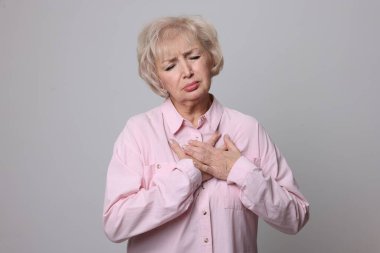 Kalp krizi geçirdi. Gri arka planda göğüs ağrısı çeken yaşlı bir kadın.