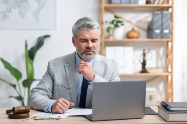 Ofiste dizüstü bilgisayarla çalışan takım elbiseli noter.