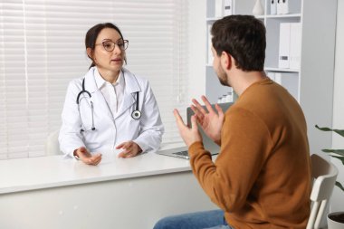 Klinikteki beyaz masada hastayla çalışan bir doktor.