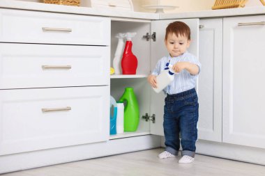 Evde çocuk güvenliği. Küçük çocuk mutfakta temizlik ürünleriyle dolap açıyor.