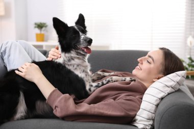 Evdeki kanepede sevimli köpeğiyle gülümseyen kadın.