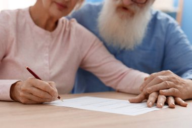 Ahşap masada son arzuları ve vasiyetnameleri imzalayan yaşlı çift, yakın plan.