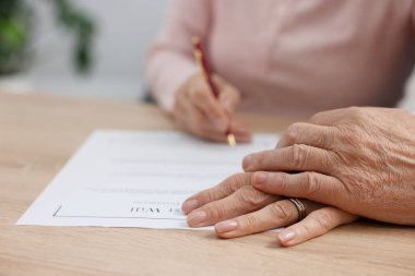 Ahşap masada son arzuları ve vasiyetnameleri imzalayan yaşlı çift, yakın plan.