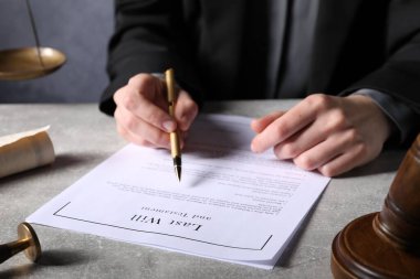 Woman signing Last Will and Testament at grey table, closeup
