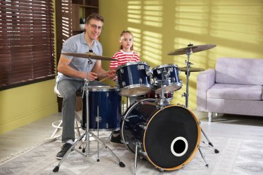 Küçük kız içeride müzik öğretmeniyle davul çalmayı öğreniyor.