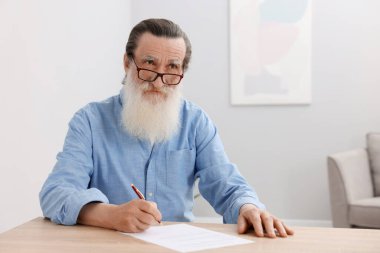 Ahşap masada son dilek ve vasiyetnameyi imzalayan kıdemli bir adam.