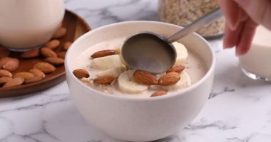 Beyaz mermer masada badem sütü, muz ve fındık ile yulaf ezmesi yiyen kadın, yakın plan.