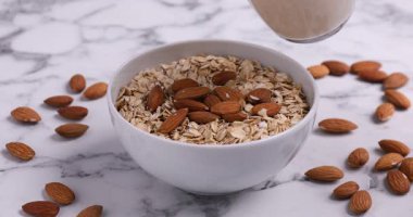 Beyaz mermer masada yulaf ezmesi ve fındıklı badem sütü döken kadın, yakın plan.