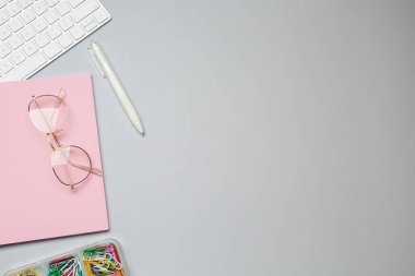 Ofis işyeri. Defter, gözlük, kalem ve klavye gri masada, düz yerde. Metin için boşluk