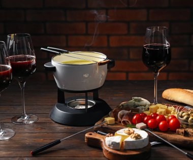 Kapalı masa üzerinde eritilmiş peynir, şarap ve atıştırmalıklar ile fondü tenceresi (caquelon)