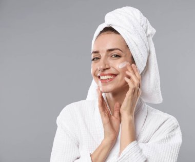 Saçları havluya sarılı güzel bir kadın ve yüzü gri arka planda kozmetik ürünler.