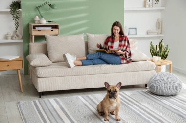 Dergisi olan bir kadın evdeki sevimli köpeğinin yanındaki kanepede dinleniyor.