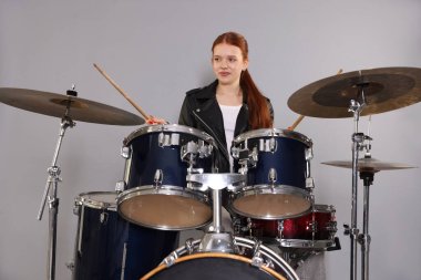 Açık gri arka planda bagetleri ve davulları olan genç bir kız.