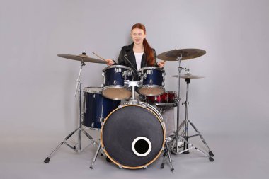 Açık gri arka planda bagetleri ve davulları olan genç bir kız.