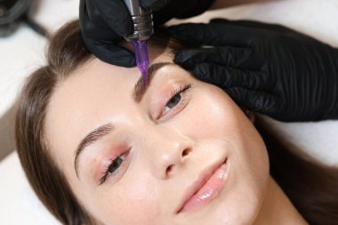 Güzellik uzmanı, genç bayana kalıcı kaş makyajı yapıyor.