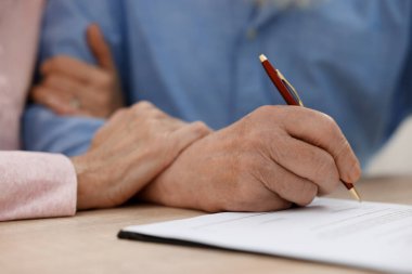 Ahşap masada son arzuları ve vasiyetnameleri imzalayan yaşlı çift, yakın plan.