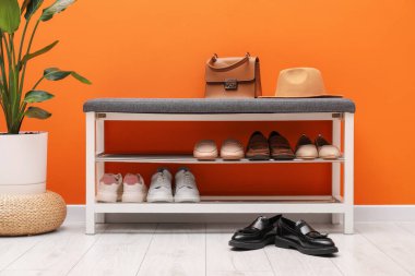 Farklı ayakkabı, aksesuarlar ve turuncu duvarın yanındaki ev bitkileriyle dolu bir ayakkabı deposu.