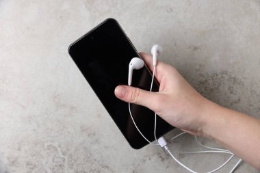 Açık gri masada akıllı telefonu ve kulaklığı olan bir kadın.