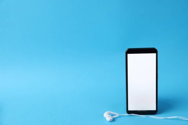 Açık mavi arka planda kulaklıklı akıllı telefon, yakın plan. Metin için boşluk