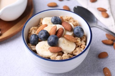 Bademli yulaf gevreği, yaban mersini, muz ve süt açık gri masada, yakın plan.