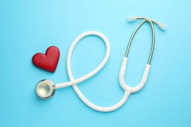 Açık mavi arka planda beyaz steteskop ve kalp modeli.