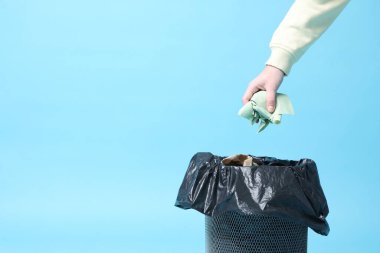 Açık mavi arka plandaki çöp kutusuna peçete atan kadın, yakın plan. Metin için boşluk