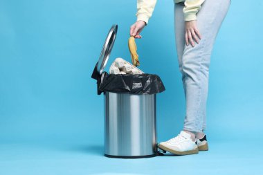 Açık mavi arka planda muz kabuğu atan kadın, yakın plan.