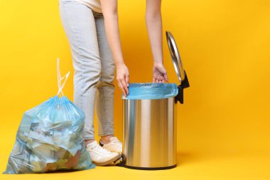 Turuncu arka plandaki çöp kutusuna plastik poşet koyan kadın, yakın plan.