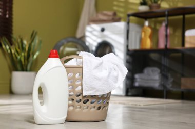 Çamaşır sepetinin içinde giysiler ve yerde deterjan var, yakın plan. Metin için boşluk