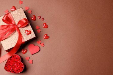 Sevgililer Günü. Hediye kutusu ve kahverengi arka planda dekoratif kalpler, düz yatış. Metin için boşluk