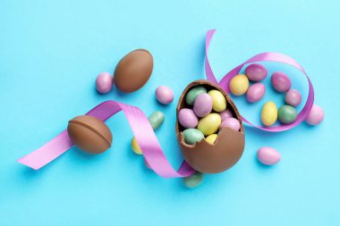 Çikolatalı Paskalya yumurtaları ve açık mavi arka planda menekşe kurdelesi.