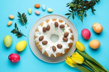 Lezzetli Paskalya pastası, boyanmış yumurtalar, güzel laleler ve açık mavi arka planda yeşil yapraklar.