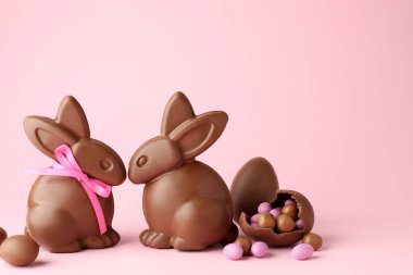 Çikolatalı Paskalya tavşanları ve pembe arka planda şekerli yumurtalar. Metin için boşluk