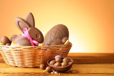 Hasır sepetin içinde yumurta ve şekerlerle bej renkli arka planda çikolatalı Paskalya tavşanı. Metin için boşluk