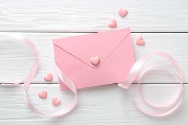 Sevgililer Günü tebrik kartı. Zarf, pembe dekoratif kalpler ve beyaz ahşap masa üzerinde kurdele.