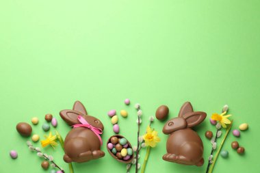 Çikolatalı Paskalya tavşanları, söğüt dalları ve açık yeşil arka planda yumurtalar, düz yatak. Metin için boşluk