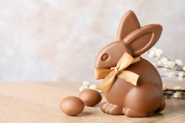 Çikolatalı Paskalya tavşanı, söğüt dalları ve tahta masada açık gri arka planda yumurtalar, yakın plan. Metin için boşluk