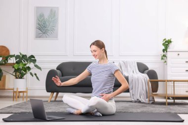 Hamile bir kadın evde dizüstü bilgisayarla yoga dersi alıyor.