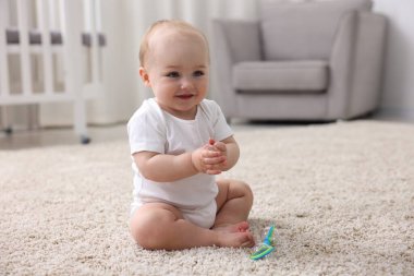 Evdeki halıda çıngıraklı oyuncağı olan şirin bir bebek.