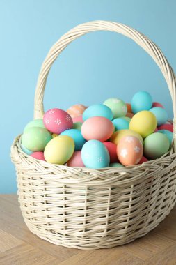 Güzel dekore edilmiş Paskalya yumurtaları hasır sepetin içinde ahşap masanın üzerinde açık mavi arka planda, yakın plan